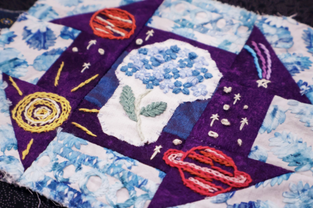Embroidered quilt square with intricate blue hydrangeas and cosmic imagery of planets
